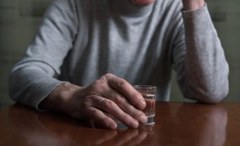 starszy mężczyzna siedzi przy stole i trzyma kieliszek z alkoholem