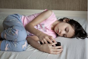 Smutna dziewczynka leży na łóżku i patrzy w telefon