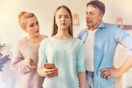 Nastolatka ze słuchawkami na uszach wygląda na sfrustrowaną, podczas gdy jej rodzice kłócą się lub ją besztają. Trzyma telefon z zamkniętymi oczami, ignorując ich - przypominając, jak trudne może to być i dlaczego warto wiedzieć, jak budować relacje z dzieckiem.