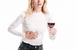 Ból wątroby po alkoholu. kobieta na białym tle trzyma kieliszek wina i chwyta się za brzuch