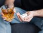 Picie alkoholu a ryzyko samobójstwa. Mężczyzna ze szklanką whisky w ręku i garścią tabletek w drugiej