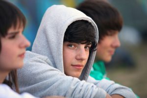 Nastolatek w szarej bluzie z kapturem patrzy w obiektyw