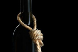 Butelka ciemnego wina z grubym, szorstkim sznurem zawiązanym na szyjce, na czarnym tle, symbolizująca uzależnienie od alkoholu.