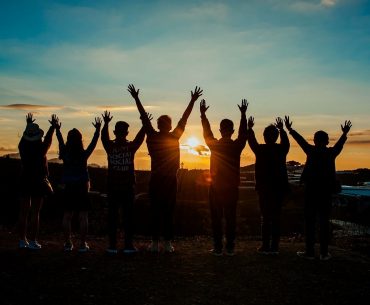 Grupa młodych z podniesionymi rękoma. w tle zachód słońca