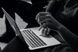 Osoba korzystająca z laptopa, z jedną ręką na klawiaturze, a drugą uniesioną, częściowo widoczna w słabo oświetlonym otoczeniu podczas przemoc bezpłatny webinar.